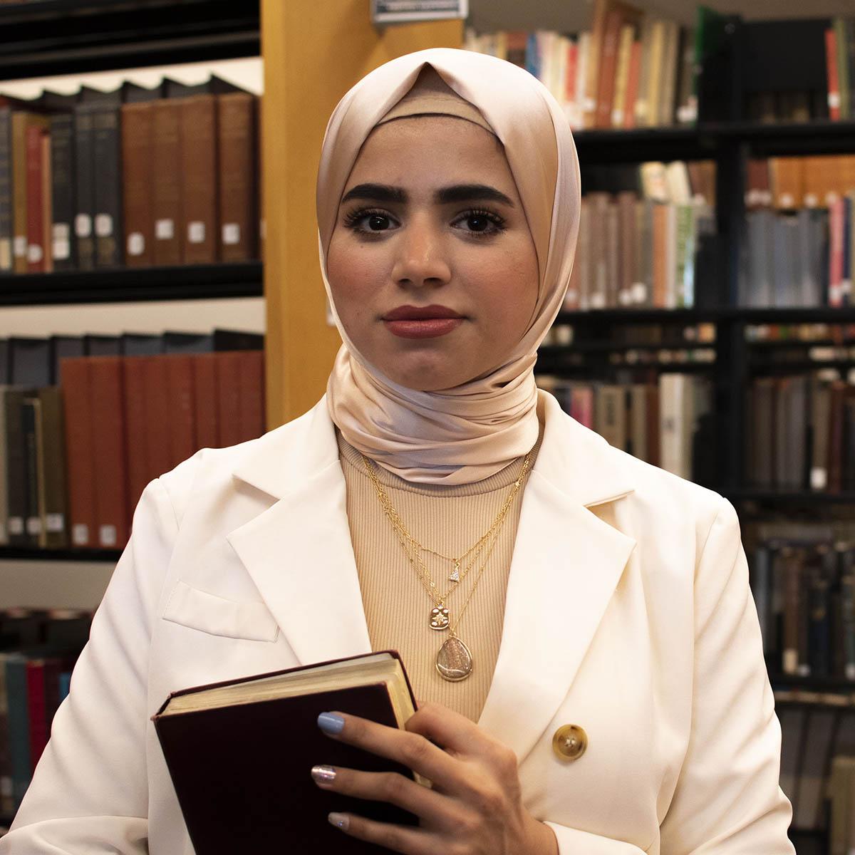 Portrait of Mural Rahim, standing in front of rows of books at the library